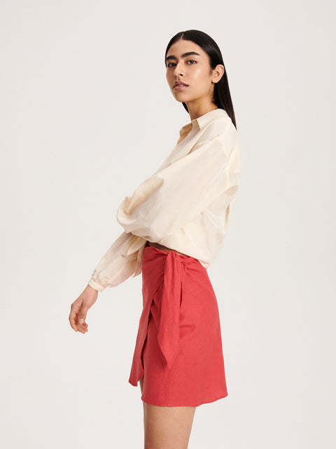 Woman wearing a cream blouse and red skirt on a white background