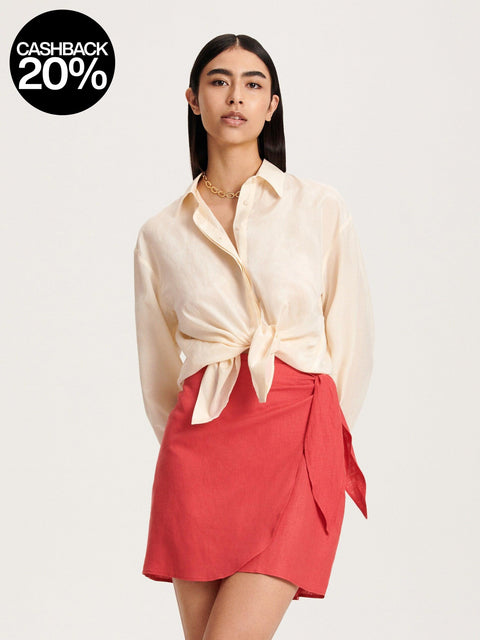 Woman wearing a cream blouse with a knot detail and a red skirt on a white background