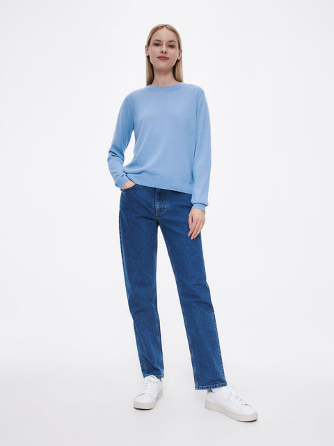 Woman wearing a light blue sweater and dark blue jeans on a white background