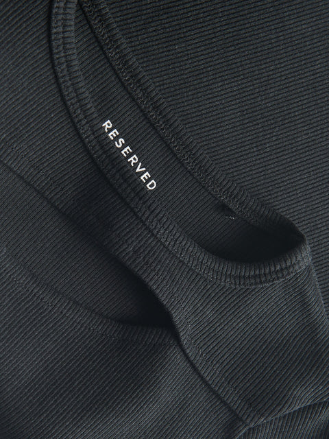 Close-up of a black garment with 'RESERVED' branding on a textured fabric background.