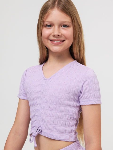 Young girl wearing a light purple textured top against a plain background