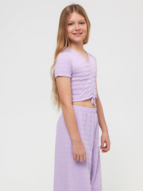 Young girl wearing a matching lavender top and skirt on a white background