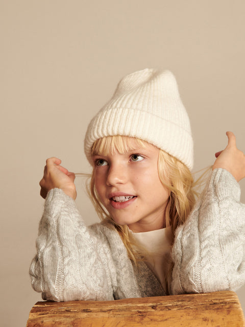 Young girl wearing a white knit hat and sweater against a beige background