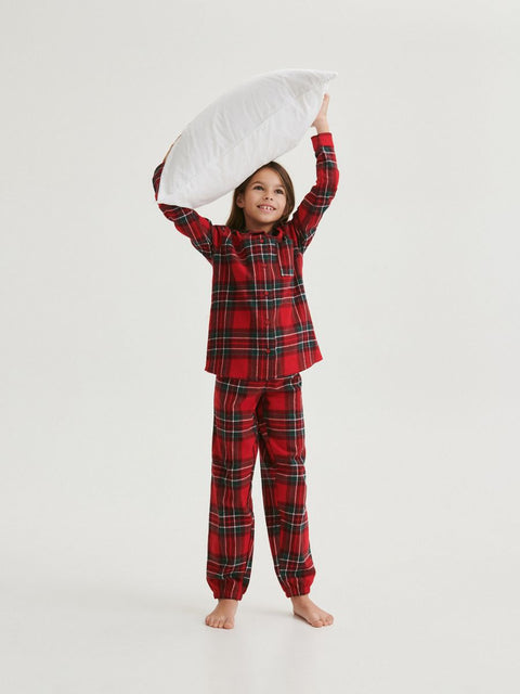 Child wearing red plaid pajamas holding a pillow on a white background