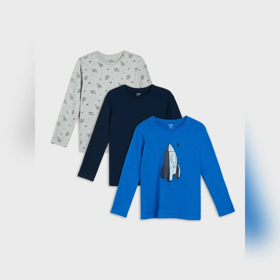 Three children's long-sleeve shirts arranged in a fan layout on a light gray background: a light gray shirt with small dark space-themed prints, a dark navy shirt, and a bright blue shirt with a large rocket graphic on the front.