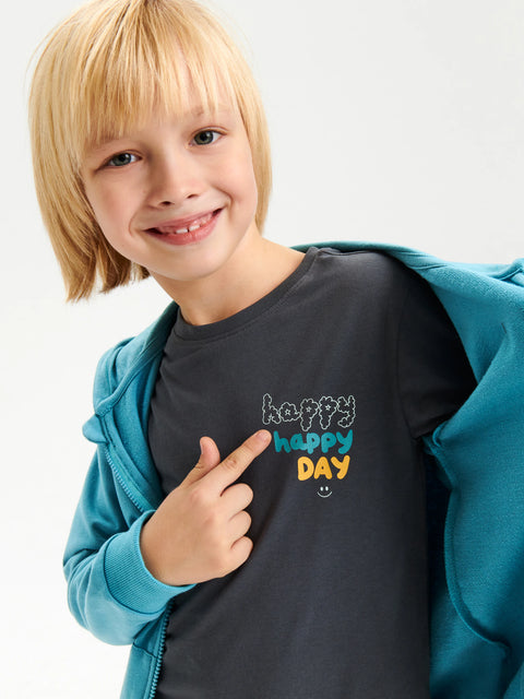 Child wearing a dark gray t-shirt with 'happy happy day' text, pointing to the shirt.