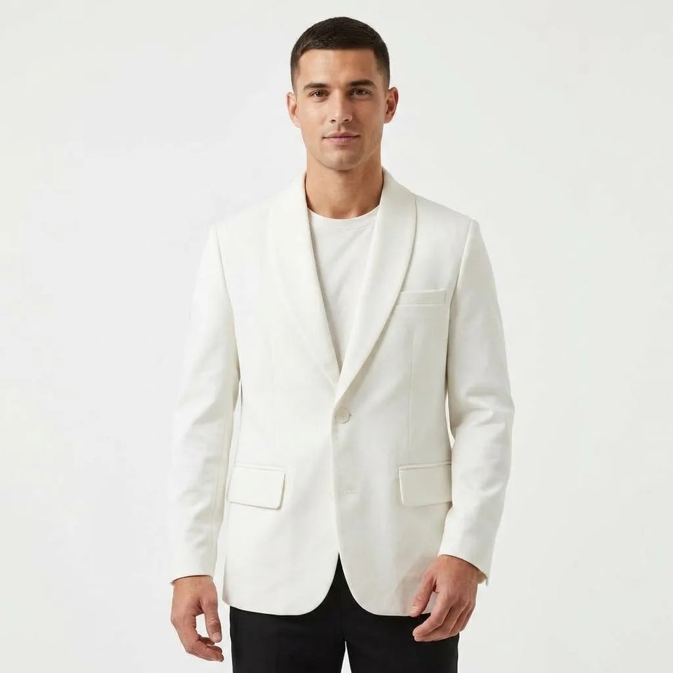 A man wearing a white shawl-collar blazer over a white t-shirt and black trousers, standing against a plain white studio background.