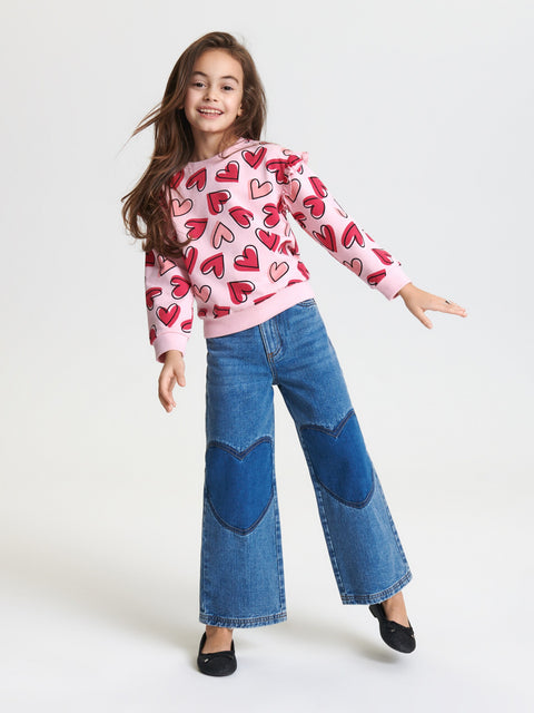 Girl wearing a pink sweater with red heart patterns and blue patchwork jeans on a white background