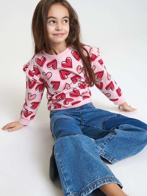 Child wearing a pink sweater with red heart patterns and blue jeans on a white background