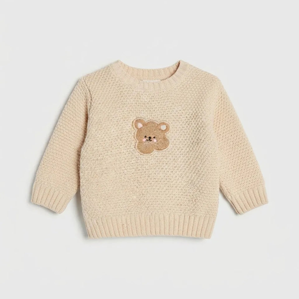 A cream-colored textured knit sweater for toddlers, featuring a small embroidered teddy bear face on the center chest, displayed against a light gray background.