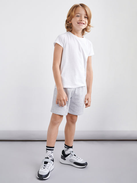 Child wearing a white t-shirt, gray shorts, and black sneakers on a plain background