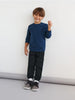 Child wearing a blue sweater and black pants against a white background