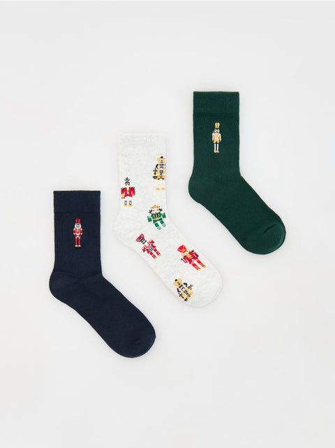 Set of three socks in black, white, and green with nutcracker designs on a light gray background.