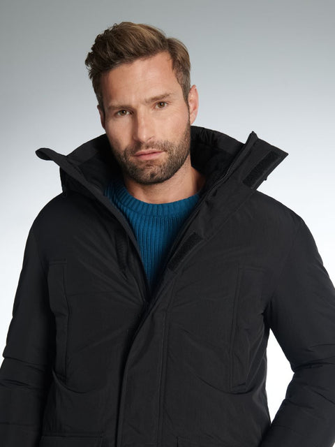 Man wearing a black coat with a hood against a gray background
