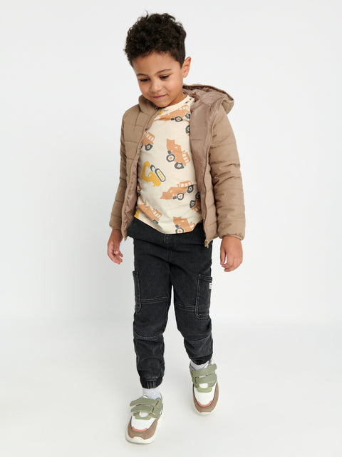 Child wearing a beige jacket, patterned shirt, black pants, and white socks with green shoes on a white background