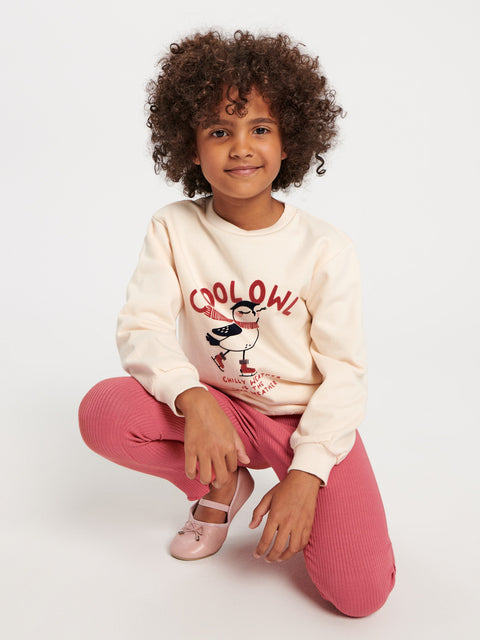 Child wearing a cream sweatshirt with text and graphics, sitting on a white background