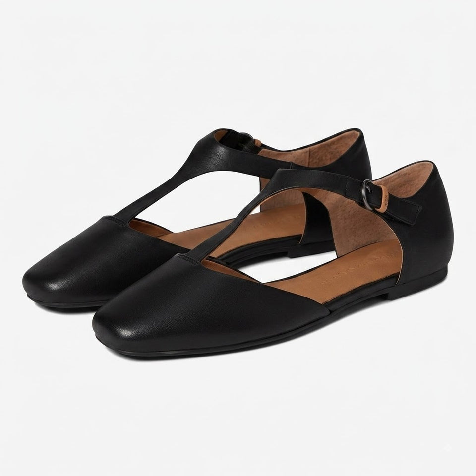 A pair of black leather flat shoes with square toes and T-strap designs, displayed on a clean white background.