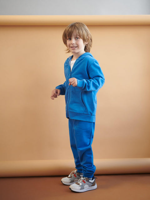 Child wearing a blue tracksuit standing against a beige background