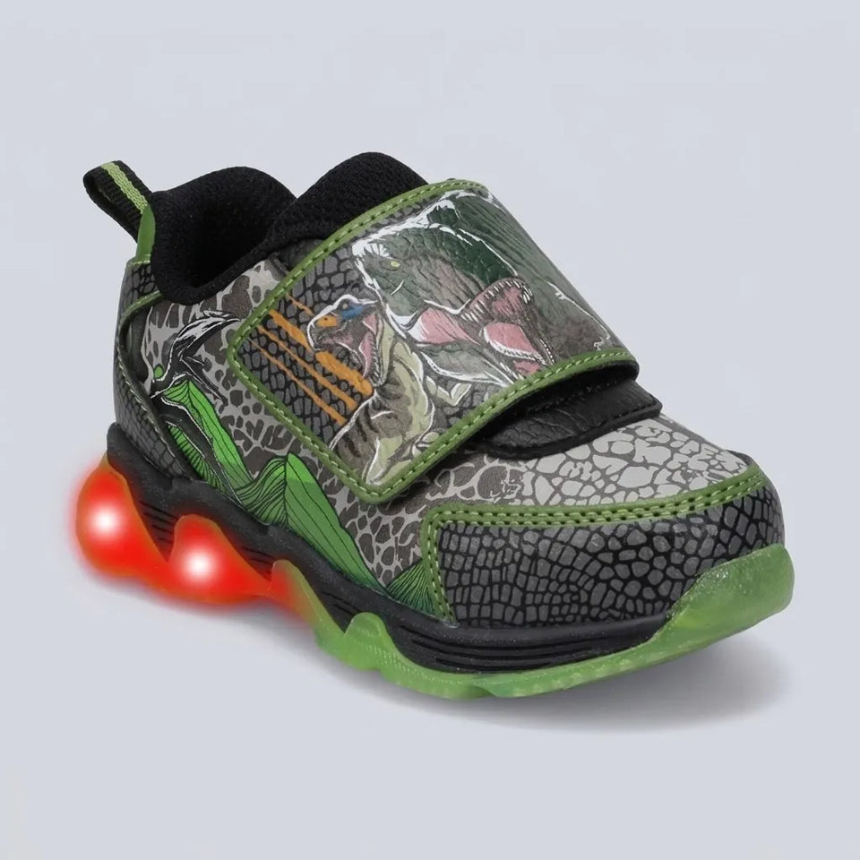 A kids' light-up sneaker with a dinosaur-themed camouflage pattern featuring green, gray, and black tones, with a glowing red LED sole on a light gray background.