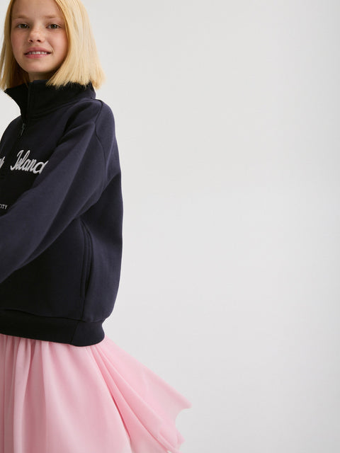 Child wearing a navy sweatshirt with text and a pink skirt on a light gray background
