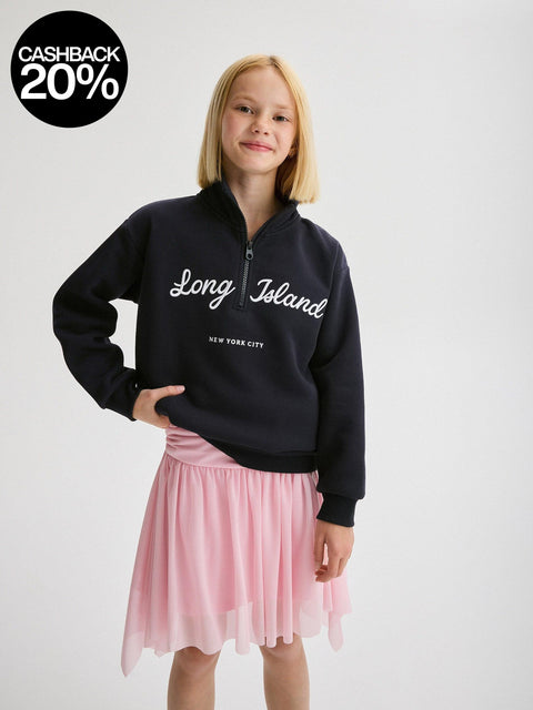 Girl wearing a black sweatshirt with 'Long Island New York City' text and a pink skirt on a white background.