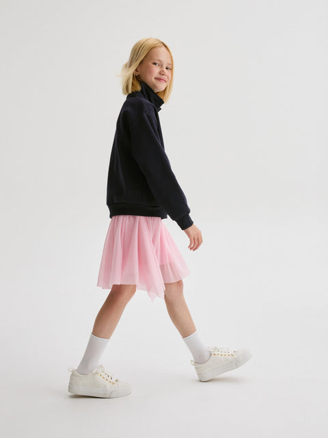 Young girl wearing a black sweater and pink skirt on a white background