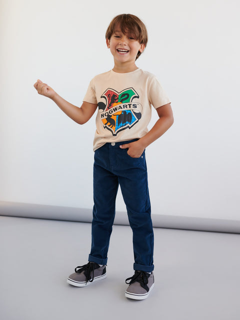 Child wearing a Harry Potter-themed t-shirt and blue jeans on a plain background