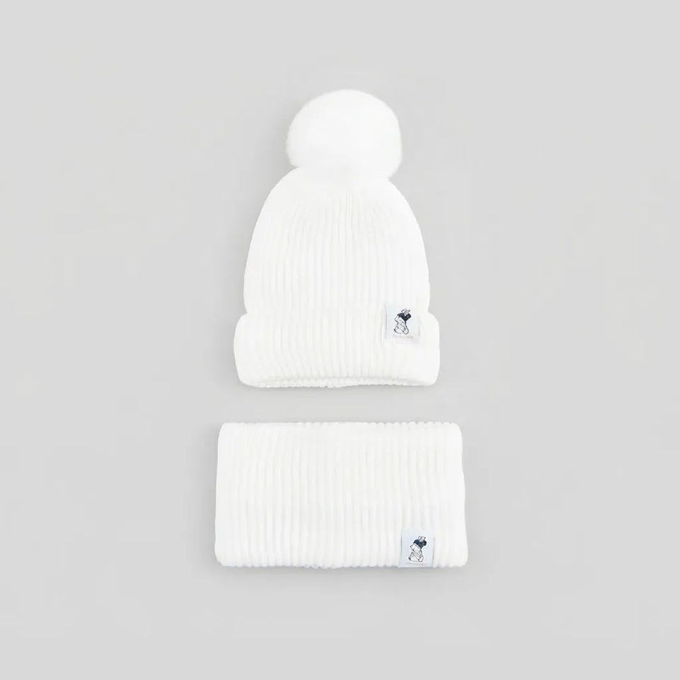 A white ribbed knit beanie with a matching pom-pom and a folded matching headband, both featuring a small navy and white logo patch on the cuff, set against a solid light gray background.