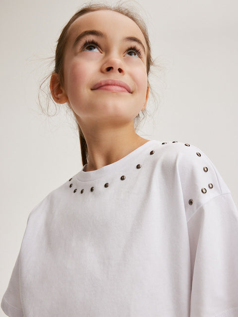 Young girl wearing a white sweatshirt with decorative studs on a plain background