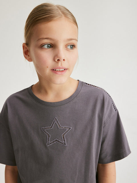 Child wearing a gray t-shirt with a star design on a plain background