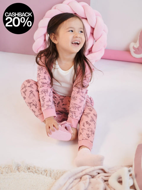 Child wearing pink pajamas with a floral pattern, sitting on a white surface.