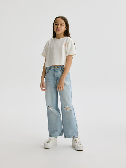 Person wearing a white t-shirt and light blue jeans on a plain background