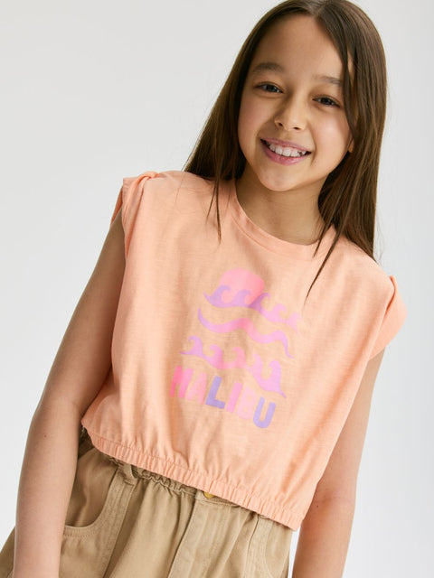 Young girl wearing a peach sleeveless top with colorful text on a white background