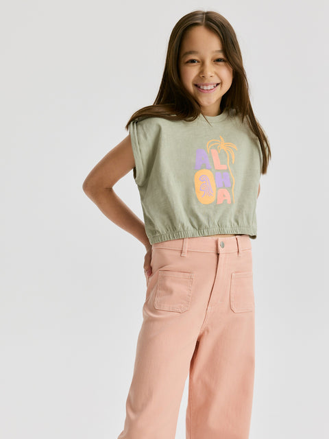 Young girl wearing a sleeveless green top with colorful letters and pink pants on a white background
