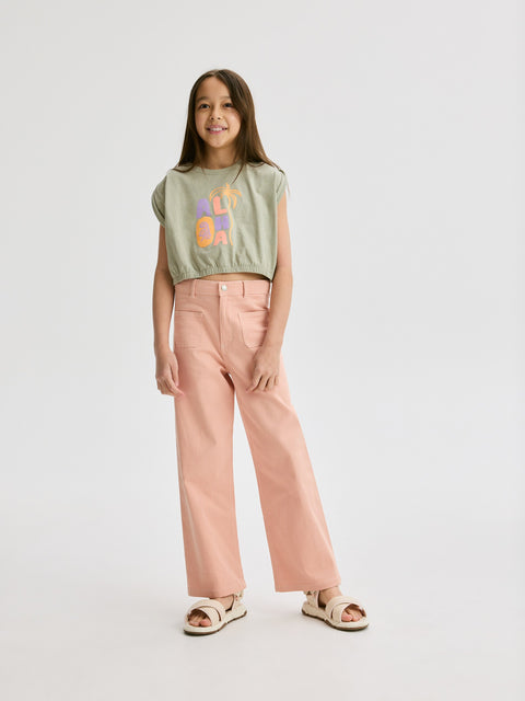 Young girl wearing a green t-shirt with colorful text and pink pants on a white background