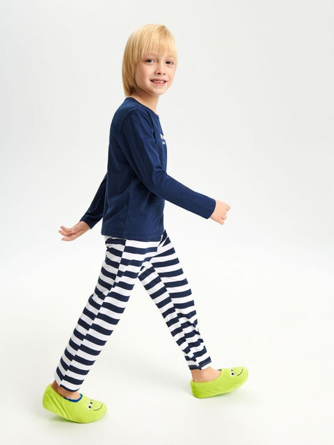 Child wearing a navy long-sleeve shirt and striped pants with green shoes on a white background