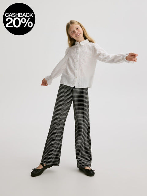 Young girl wearing a white shirt and black checkered pants on a white background