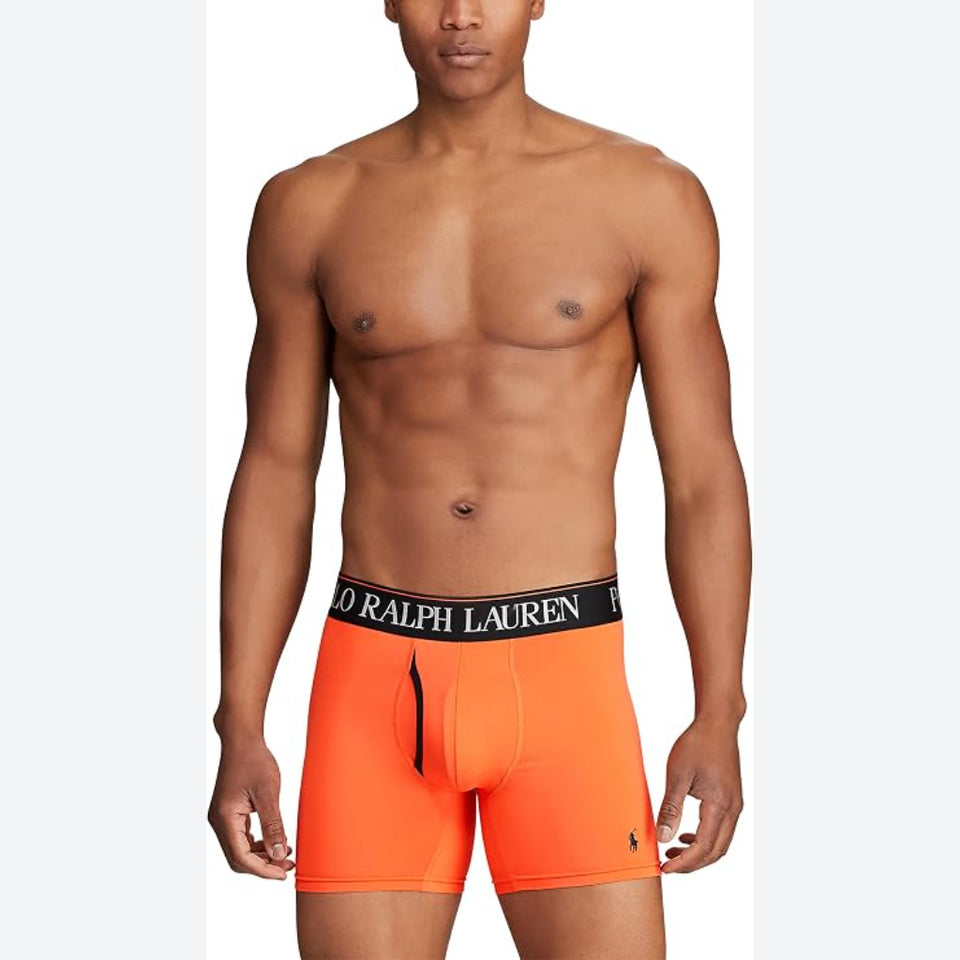 A male model wearing bright orange Polo Ralph Lauren boxer briefs with a black waistband featuring white lettering, shown against a light gray studio background.