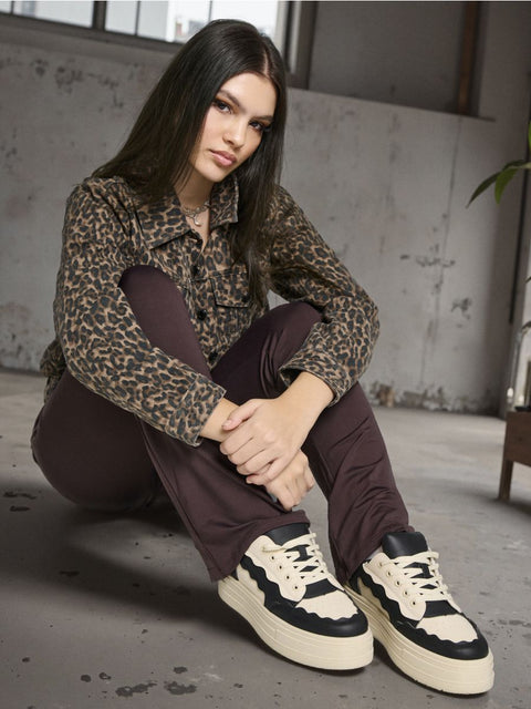 Woman wearing a leopard print jacket and brown pants sitting on the floor.