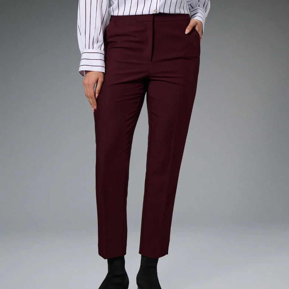 A person wearing high-waisted, straight-leg trousers in deep burgundy, paired with a white and navy striped long-sleeve shirt and black socks, shown against a neutral gray studio background.