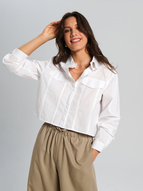 Woman wearing a white shirt and beige pants against a gray background