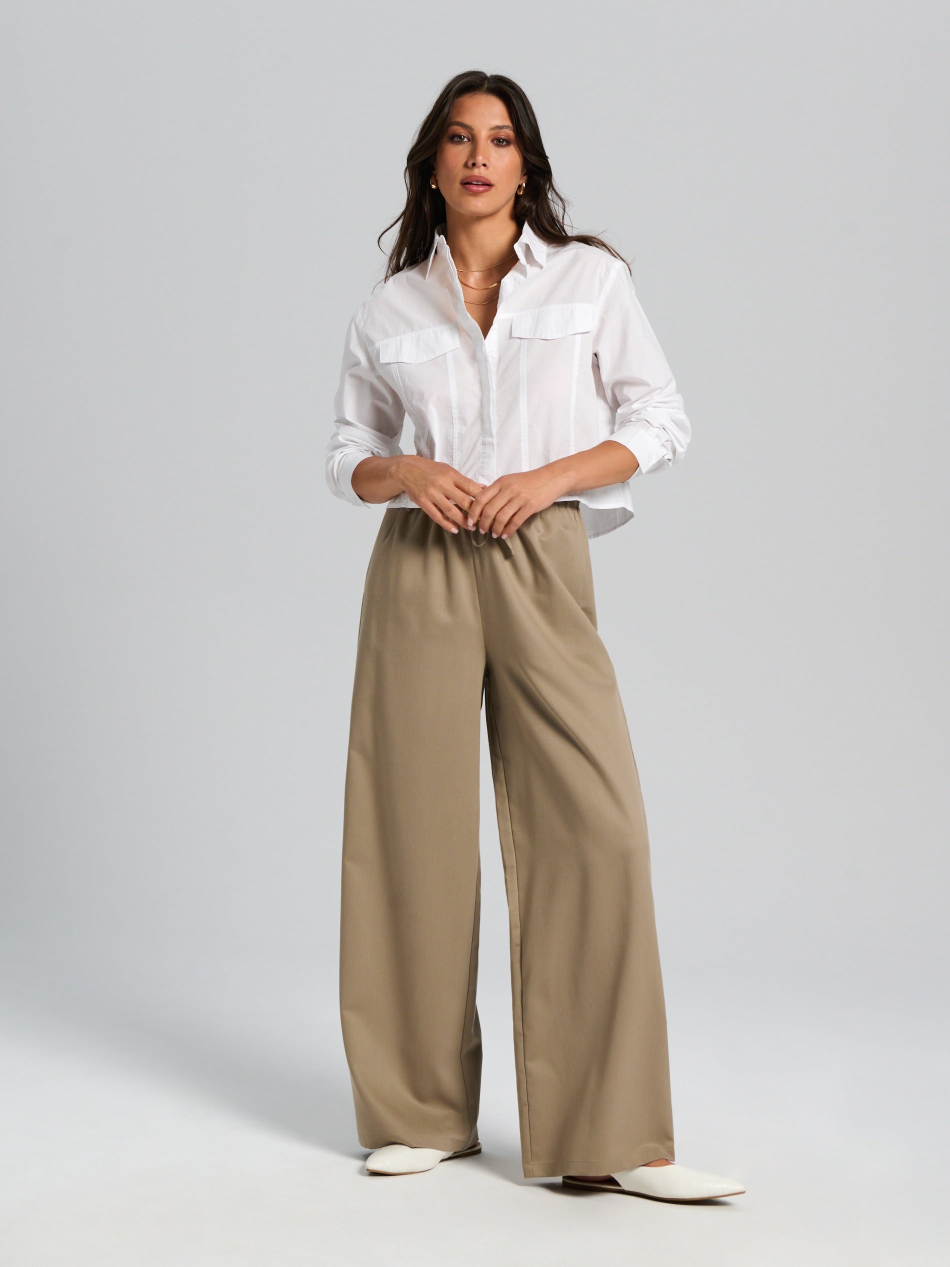 Woman wearing a white shirt and beige wide-leg pants on a gray background