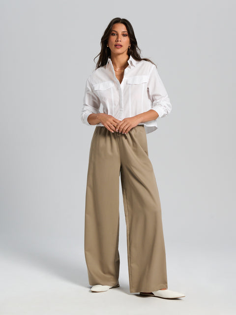 Woman wearing a white shirt and beige wide-leg pants on a gray background