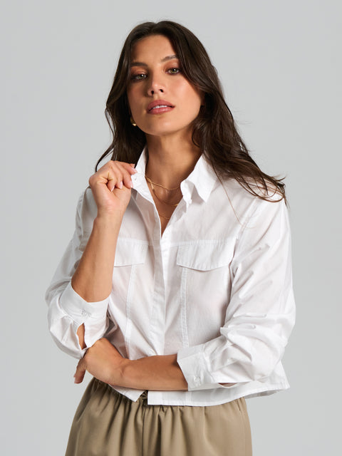 Woman wearing a white shirt with rolled-up sleeves against a gray background