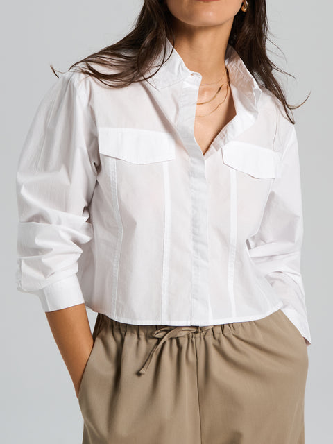 White blouse with long sleeves and a V-neckline worn by a person on a plain background