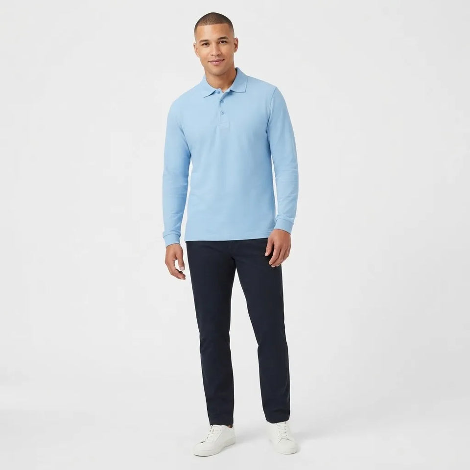 A man modeling a light blue long-sleeve polo shirt with dark navy pants and white sneakers, standing against a plain white studio background.