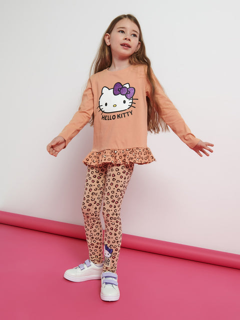 Young girl wearing a Hello Kitty outfit with a peach top and leopard print pants on a pink floor.