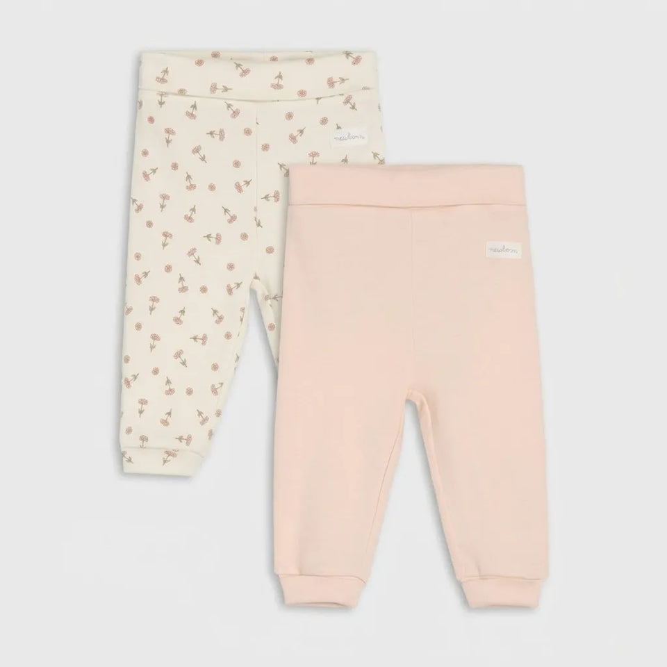 Two pairs of toddler leggings laid flat on a light gray background. The pair on the left is cream with a small pink cherry print, and the pair on the right is solid pale pink.