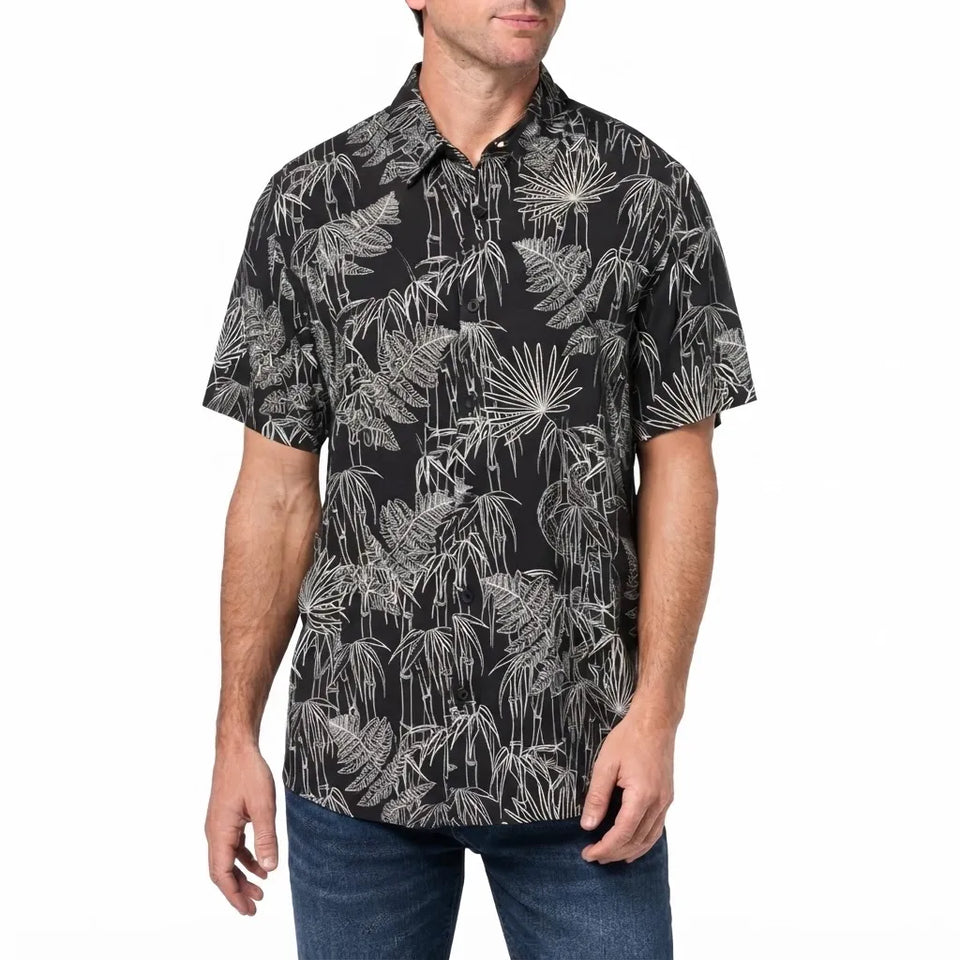 A man wearing a short-sleeve button-up shirt with a black background and a white tropical leaf print, paired with blue jeans, against a plain white background.
