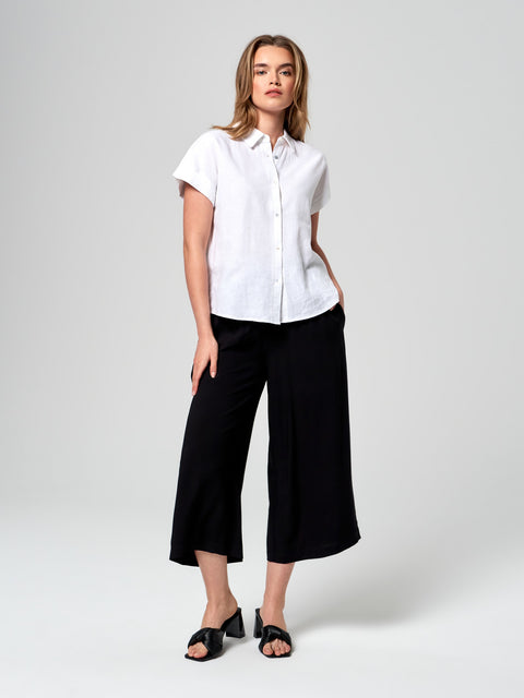 Woman wearing a white shirt and black pants on a plain background
